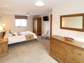 A bedroom with a bed, a wooden dresser, a chair, a television, and a window with a curtain.
