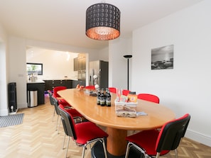 A dining area with a wooden table, red chairs, and a black pendant light. - Beach House (Bridlington)