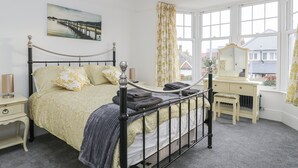 Une chambre à coucher comprenant un lit, une table de chevet, une commode, un miroir et une fenêtre avec des rideaux.