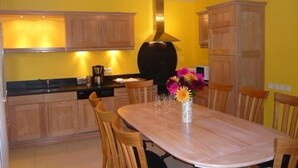A compact kitchen with wooden cabinets and a central island, a dining table with chairs, and a vase with flowers.