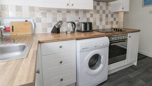 A compact kitchen with white cabinetry, a wooden countertop, a built-in washing machine, and a gas stove. - Halcyon Annexe (Moelfre)