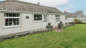 A two-story house with a stone facade, white windows, and a stone wall with spherical ornaments. - Halcyon Annexe (Moelfre)