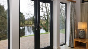 A room with a large sliding glass door leading to a wooden deck and a lake view. - Tarn Lodge (Windermere)