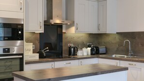 A modern kitchen with white cabinets, a built-in oven, a microwave, a toaster, and a coffee maker. - Tarn Lodge (Windermere)