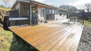 A modern wooden house with a deck, large sliding glass doors, and a hot tub. - Tarn Lodge (Windermere)