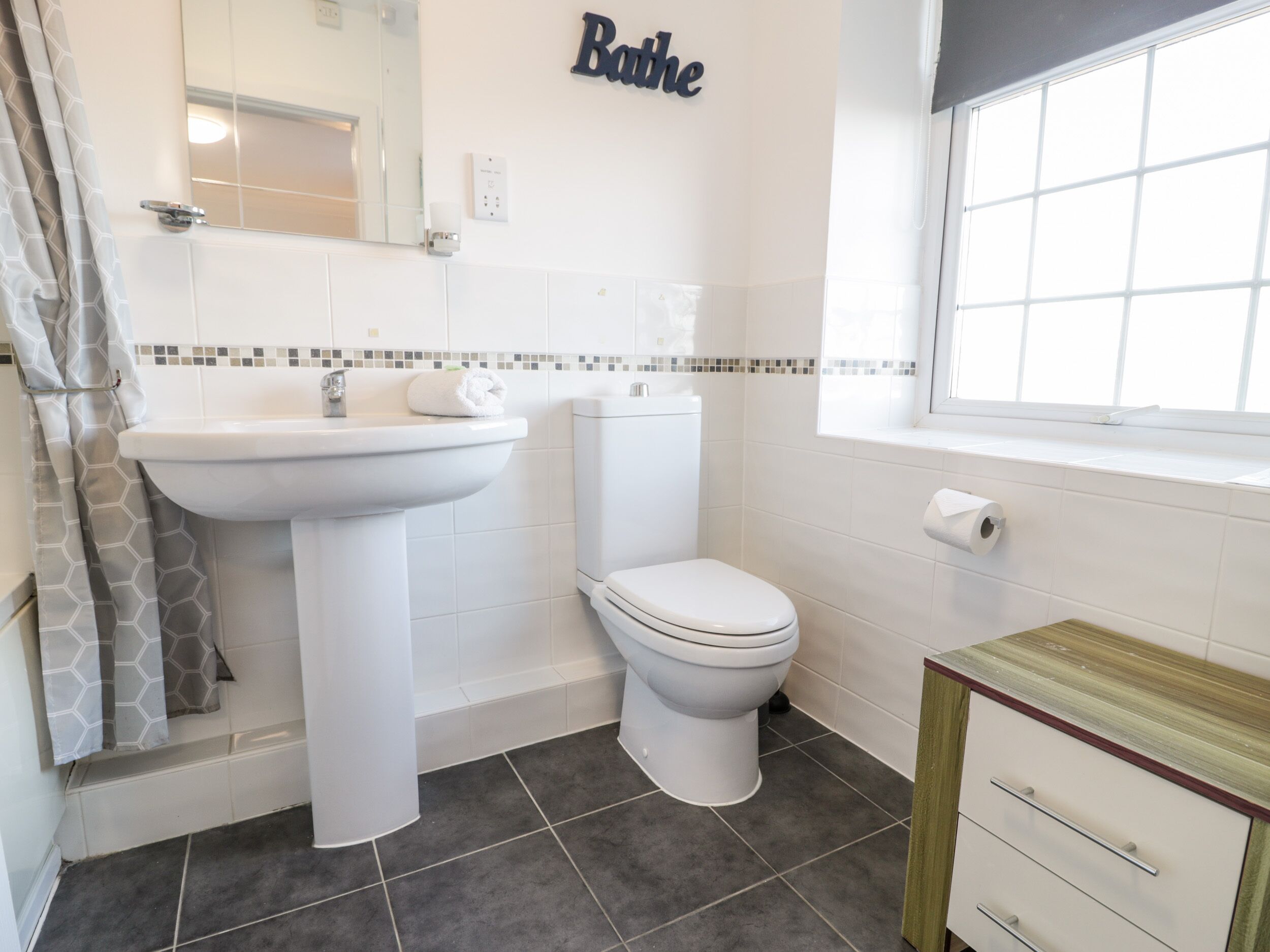 A bathroom with a sink, toilet, and a wooden cabinet.