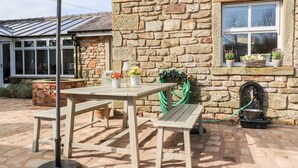 A stone building with a window, a table with chairs, and a green umbrella. - The Boot Room (Preston)