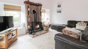 Ein gemütliches Wohnzimmer mit Kamin aus Backsteinen, einer Ledersofa, einem Flachbildfernseher und einem Bücherregal.