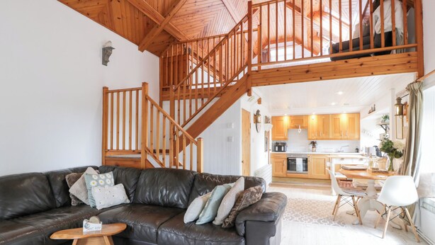 Ein gemütliches Wohnzimmer mit Ledersofa, Holztisch und einer Treppe, die in eine obere Etage führt.