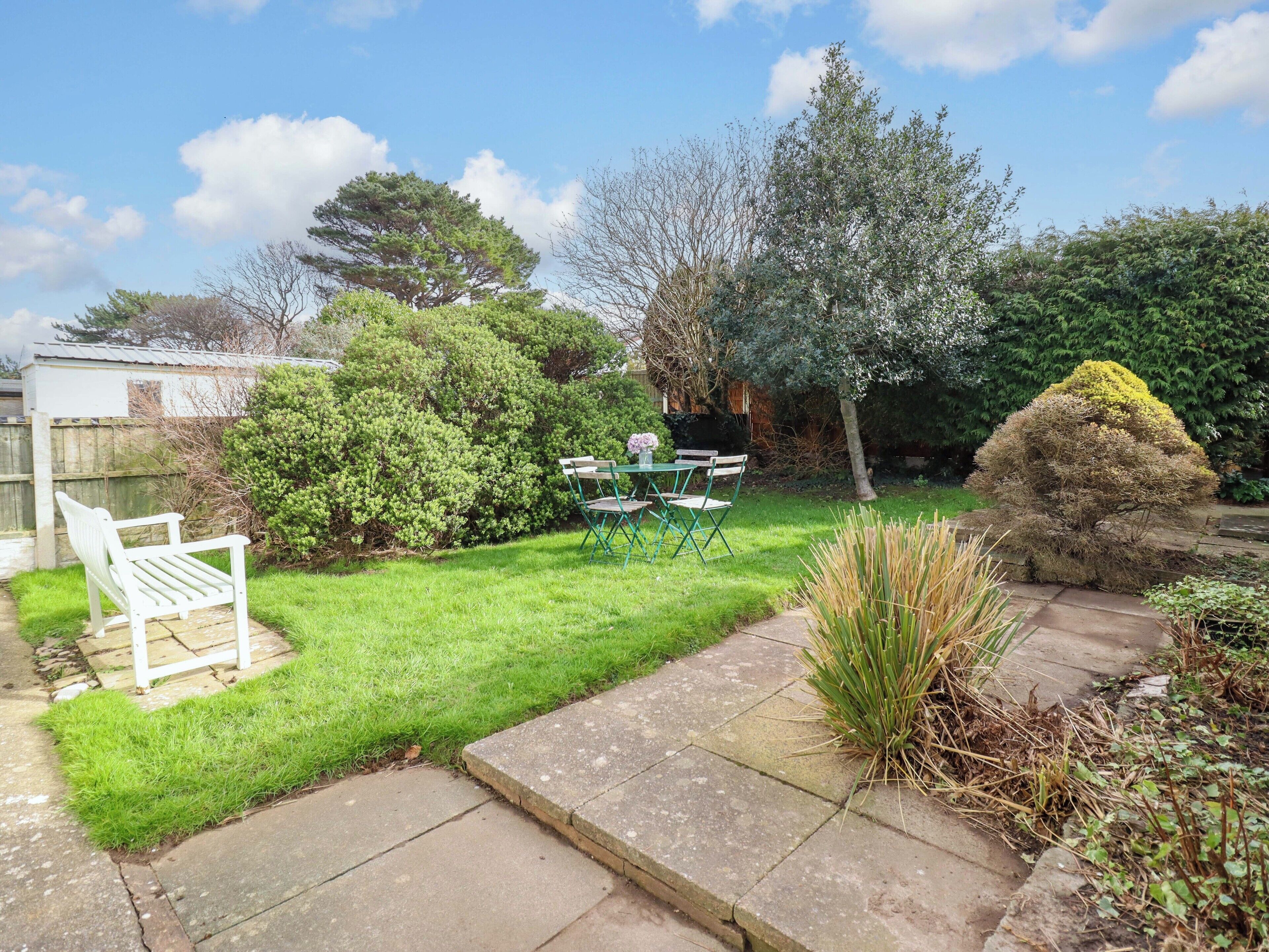A garden with a lawn, a white bench, and a table with chairs.