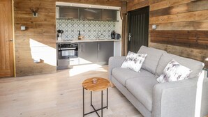 A modern kitchen with wooden walls, a grey sofa, and a small wooden table. - Deer Lodge (Wimborne)