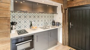A modern kitchen with wooden beams, a patterned backsplash, and stainless steel appliances. - Deer Lodge (Wimborne)