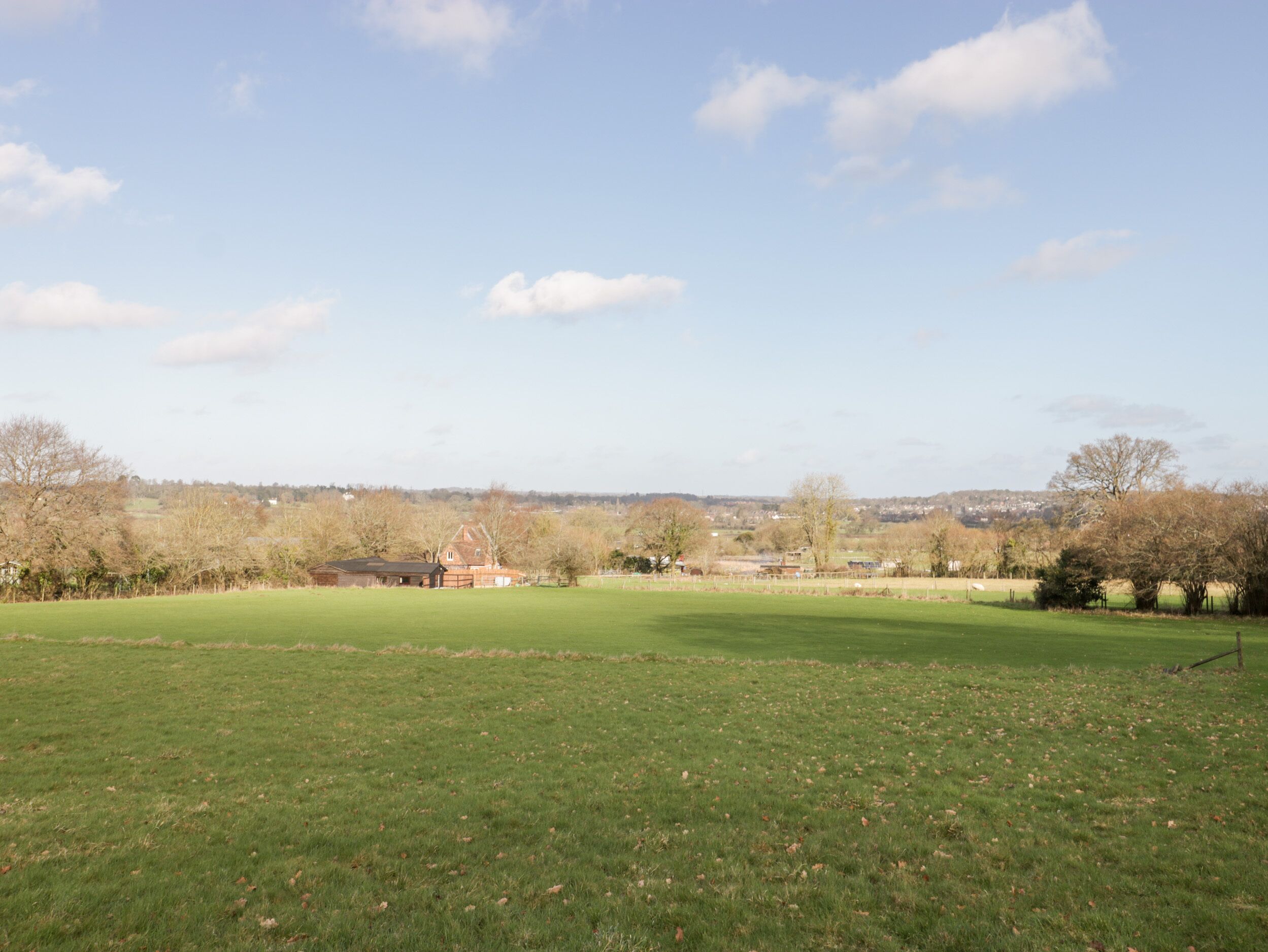 A large open grassy field with a few buildings in the distance.