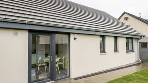 A modern house with a flat roof, large sliding glass doors, and a small patio area. - Skoglendi (Boat of Garten)