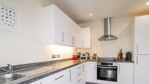 A modern kitchen with white cabinets, a stainless steel range hood, and a granite countertop. - Skoglendi (Boat of Garten)