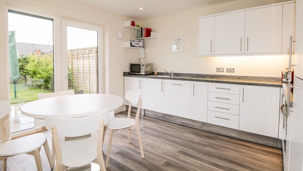 A modern kitchen with white cabinets, a round dining table, and a view of the backyard. - Skoglendi (Boat of Garten)