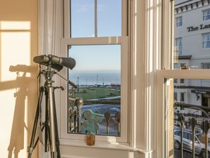 A telescope set up on a window sill, overlooking a coastal view with a building labeled "The Langley" in the background.