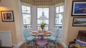 A corner room with a bay window, a dining table with chairs, a radiator, and framed pictures on the walls. - Apartment 4 (Whitby)