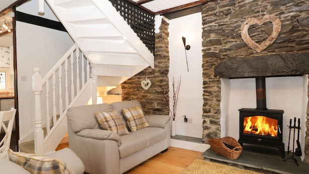 A cozy living room with a stone fireplace, a sofa, and a staircase. - Dalesway Cottage (Windermere)
