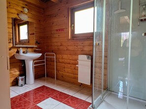 Une salle de bain rustique, aménagée dans une cabane en bois, avec un lavabo, un miroir et une douche.