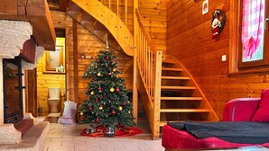 L’intérieur d’un chalet chaleureux, avec un escalier en bois, un sapin de Noël et un canapé rouge.