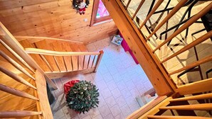 Un escalier en bois mène à un niveau inférieur où se trouvent un petit sapin de Noël et une couverture rouge sur le sol.