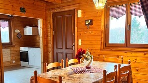 L’intérieur d’un chalet en bois comprend une table à manger, des chaises, un coin cuisine et une fenêtre avec des rideaux.