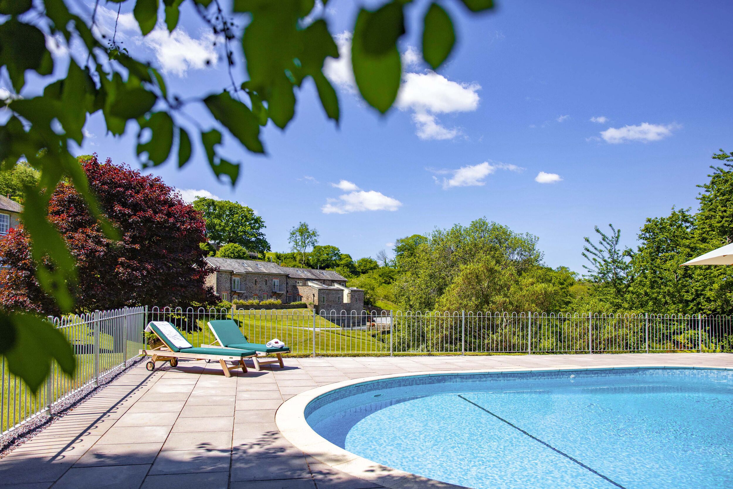 A swimming pool with two lounge chairs, a fenced area, and a stone building in the background.