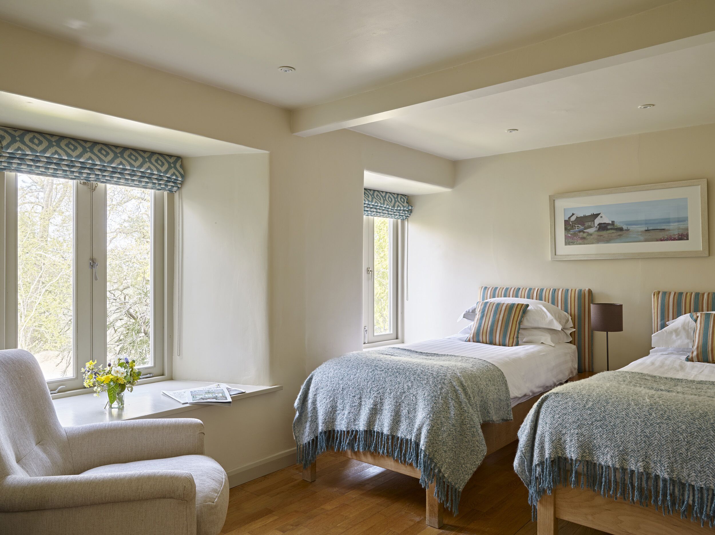 A bedroom with two beds, a window with a view, a chair, and a painting on the wall.