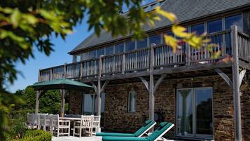 A stone building with a balcony, outdoor seating, and a pool area.