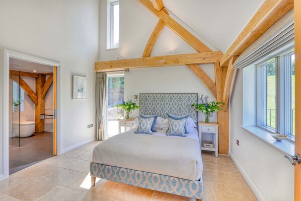 A bedroom with a large bed, wooden beams, a window, and a view of the outdoors.
