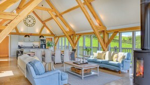 Un loft espacioso con techos altos, vigas de madera a la vista, una zona de cocina, un salón con sofás y chimenea, y ventanas grandes con vistas al exterior.
