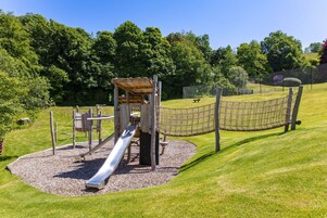 Un parque infantil con un tobogán, estructuras para escalar y una zona cercada.