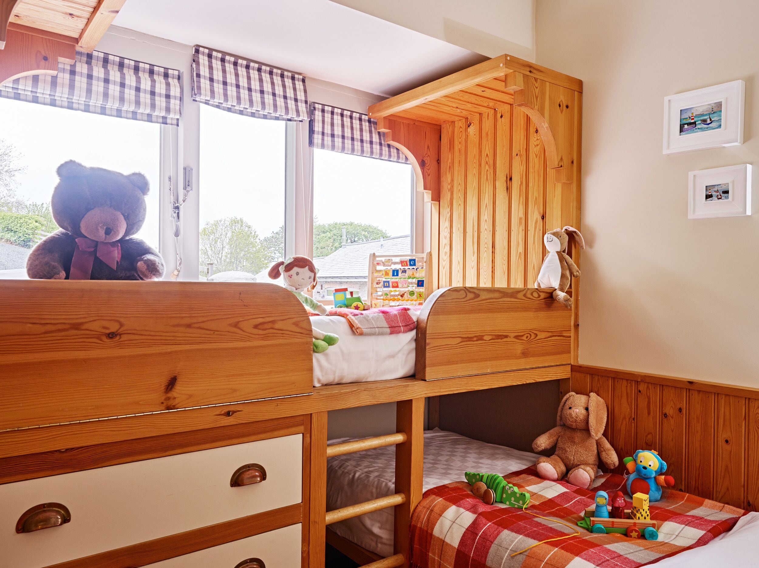 A cozy children's room with a bunk bed, wooden walls, and a window with plaid curtains.