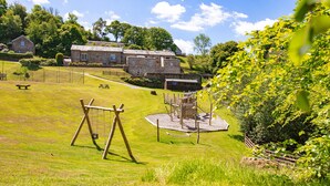 A stone building with a grassy field, a swing set, and a playground. - Garden House (Totnes)