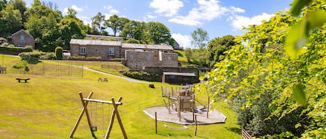 A stone building with a grassy field, a swing set, and a playground.