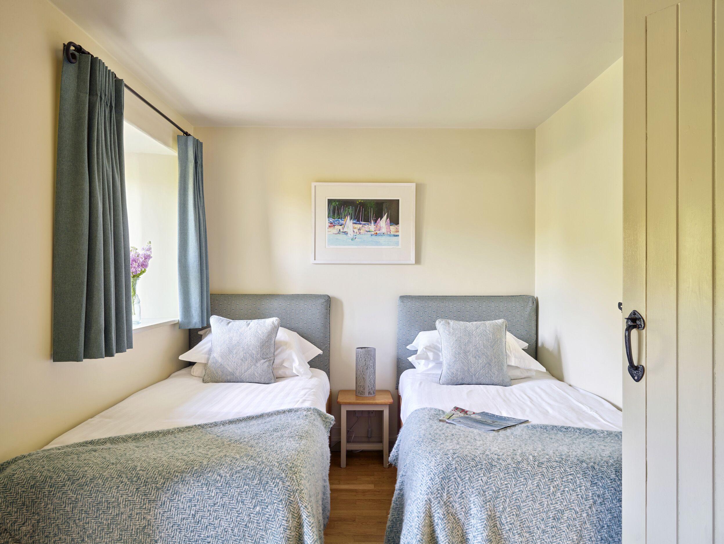 A double room with two beds, a nightstand, a framed picture on the wall, and a window with curtains.
