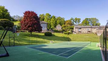 Una cancha de tenis con red, rodeada por un césped verde y un edificio de piedra.