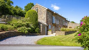 A stone house with a sloped roof, a small balcony, and a gravel driveway. - Maristow Cottage (Totnes)
