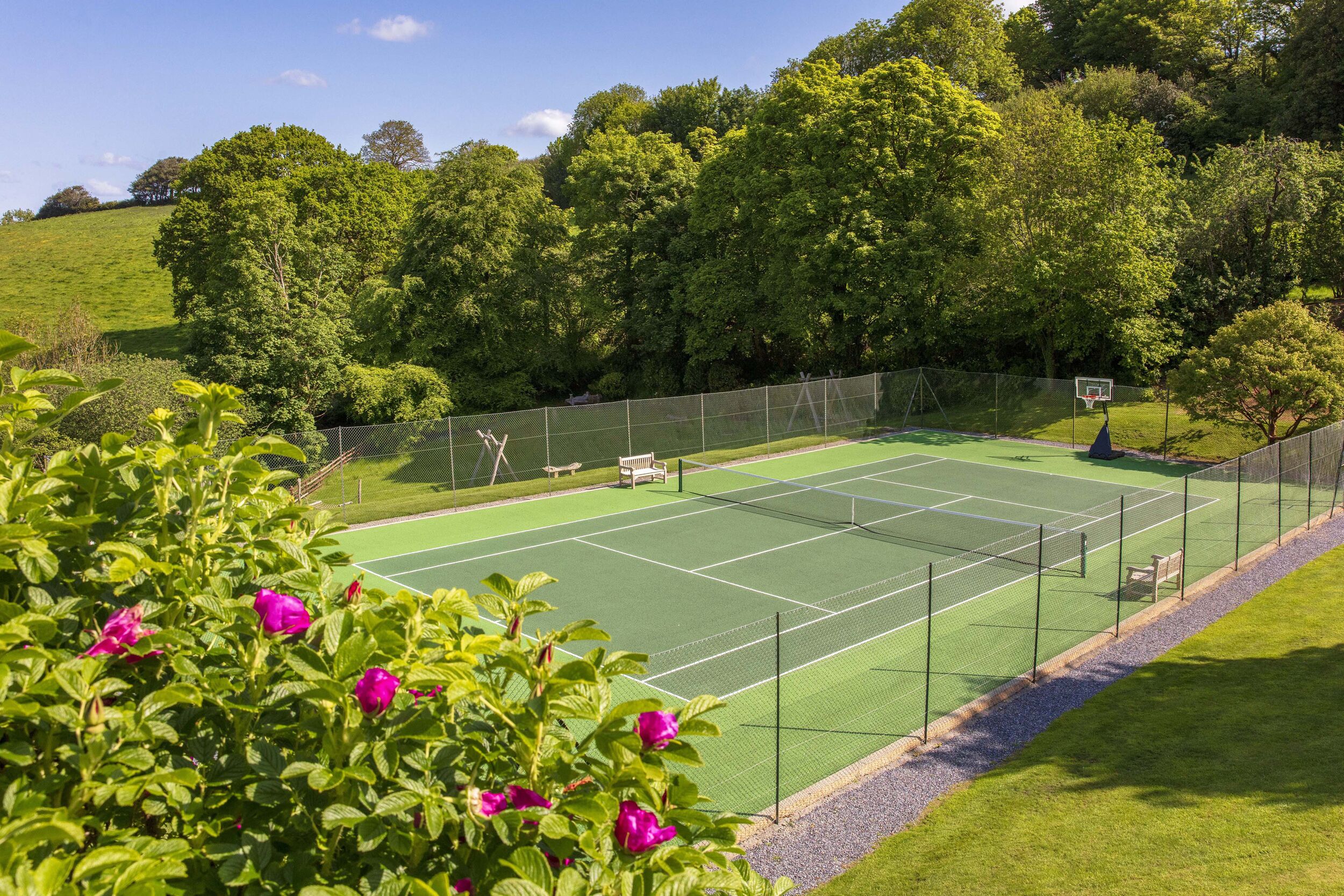 A tennis court with a net, surrounded by a fence and trees.