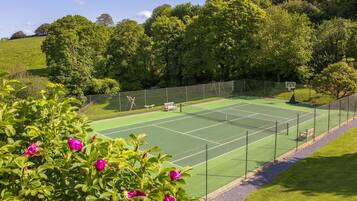 A tennis court with a net, surrounded by a fence and trees.