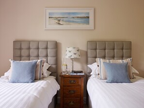 A hotel room with two beds, a nightstand with a lamp, a framed picture on the wall, and a wooden dresser with drawers. - Gitcombe House (Totnes)