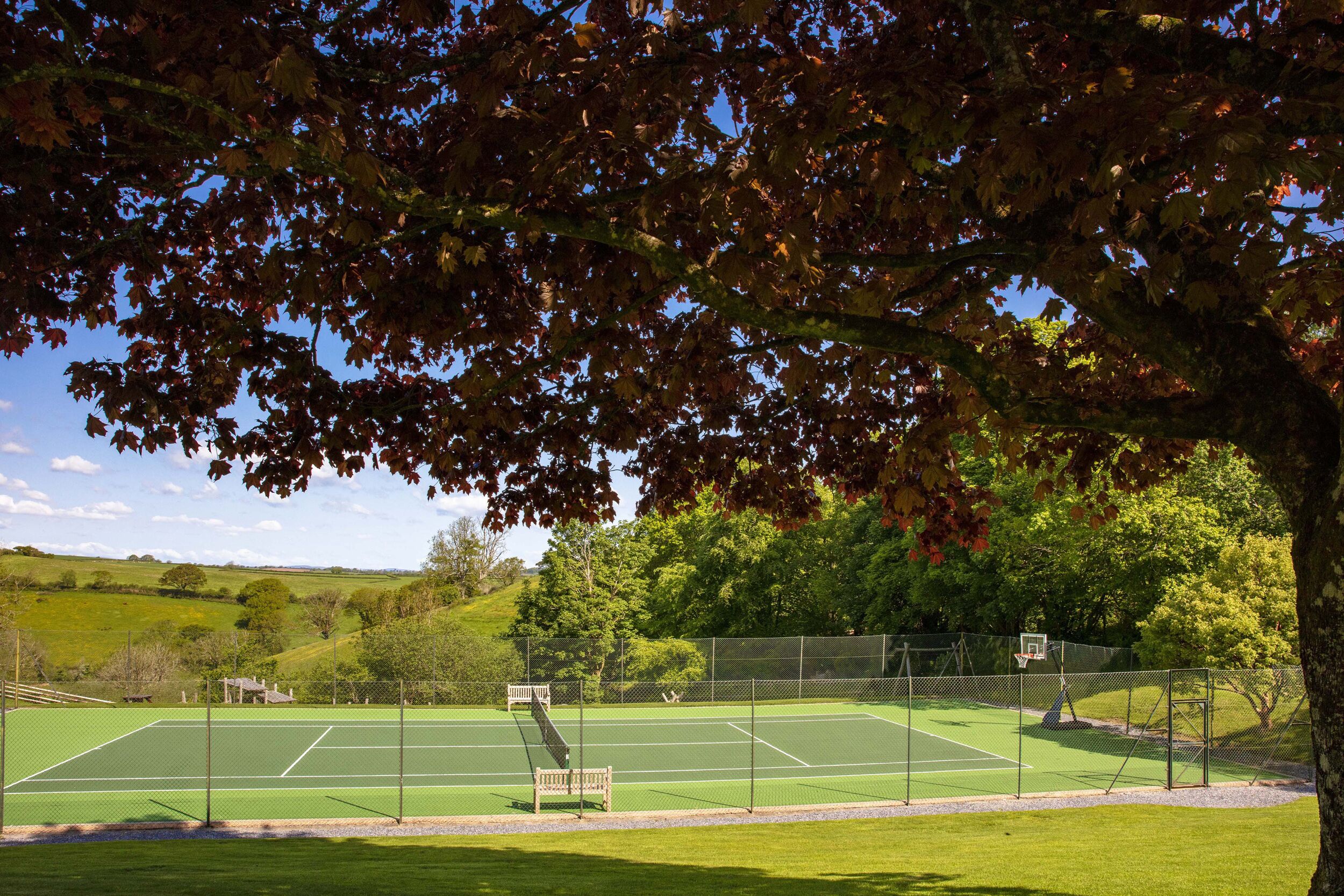 An outdoor tennis court with a net, surrounded by a fence, and a bench in the foreground.