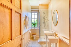 A bathroom with a wooden door, a toilet with a wooden seat, a shower area, and a sink with a mirror. - Gitcombe House (Totnes)