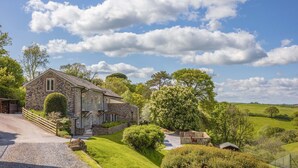 A stone house with a stone staircase, surrounded by lush greenery and a clear blue sky. - Meavy Cottage (Totnes)