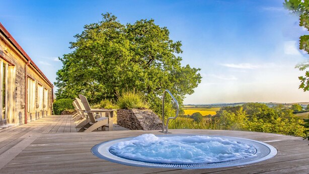 A wooden deck with a hot tub, outdoor seating, and a view of a tree and landscape. - Meavy Cottage (Totnes)