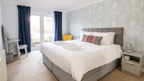 A bedroom with a bed, a nightstand, a chair, a desk, and a view of the outdoors. - Honeybees Haven (Hunstanton)