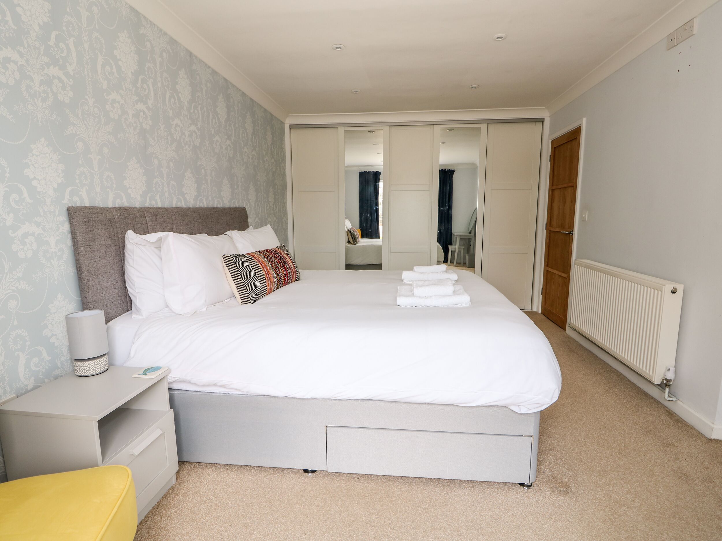 Un dormitorio ordenado con cama, mesita de noche y una silla.