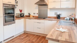 Eine moderne Küche mit weißen Schränken, einem Doppelbackofen, einer Mikrowelle, einer Edelstahl-Dunstabzugshaube und einer Holz Arbeitsplatte.