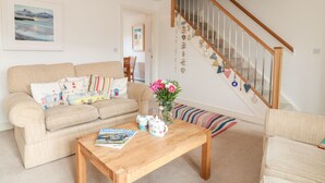 Ein Wohnzimmer mit einem beigefarbenen Sofa, einem Holztisch und einer Treppe mit einem Holzgeländer.